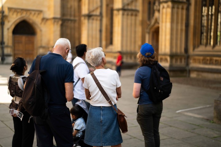 Group of people with backpacks stand outside historic building.