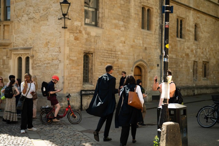 People walking and biking near a stone building on a sunny day.