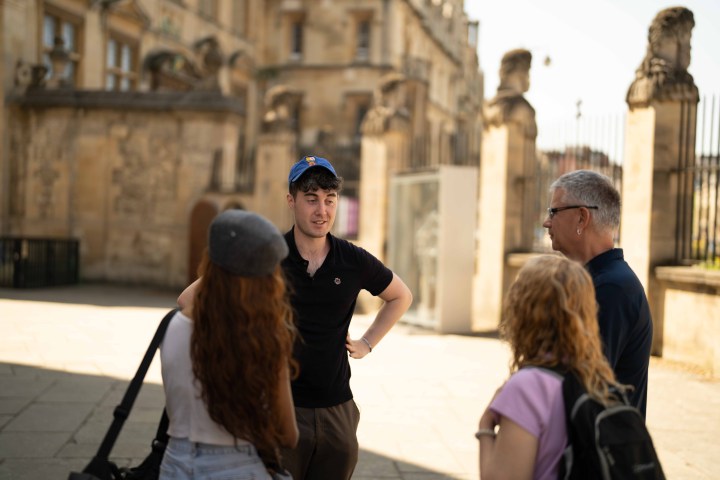 Four people talking outside a historic building on a sunny day.