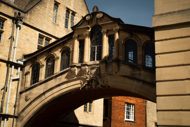 Historic stone architectural bridge between buildings under a bright sky.