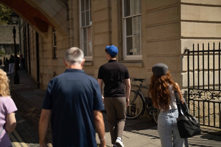 People walking on a sidewalk near a historic building with a bicycle leaning against it.