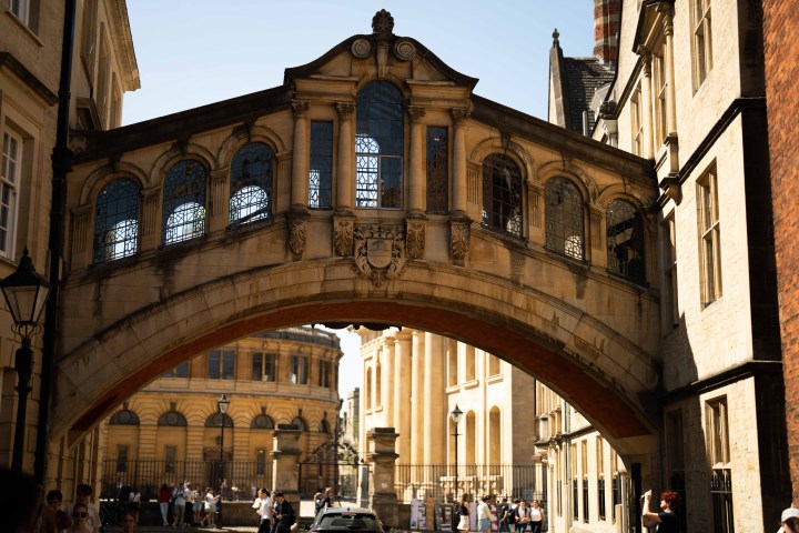 Historic arched bridge connecting two buildings under a clear sky, with people walking below.