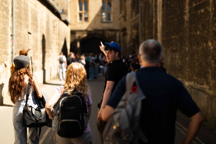 People walking down a narrow, sunlit street with one person looking back.