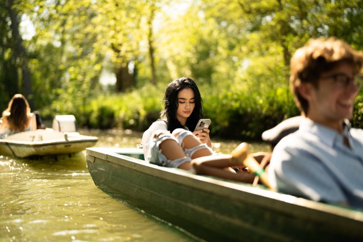 People relaxing in boats on a sunny day, one woman looking at her phone.