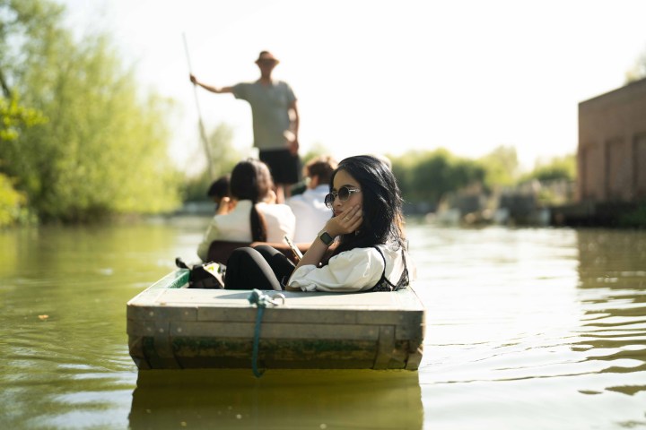 People on a small boat in a calm river with a guide standing and rowing.