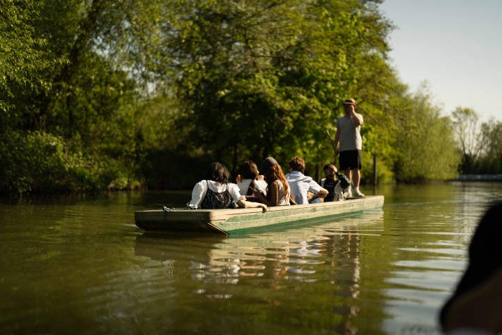 People on a boat being guided through a tranquil, tree-lined river.